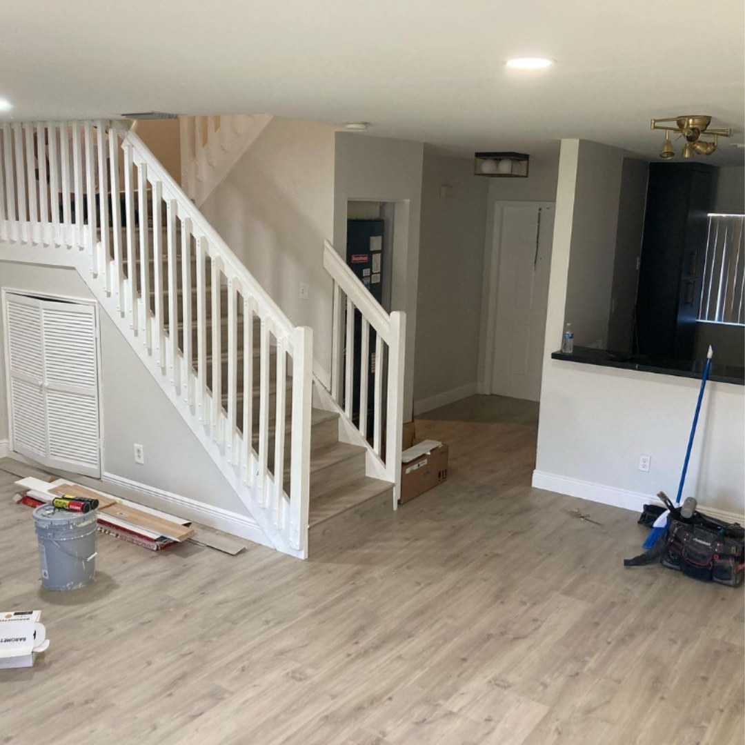 Light vinyl plank flooring in an open living area with a white staircase