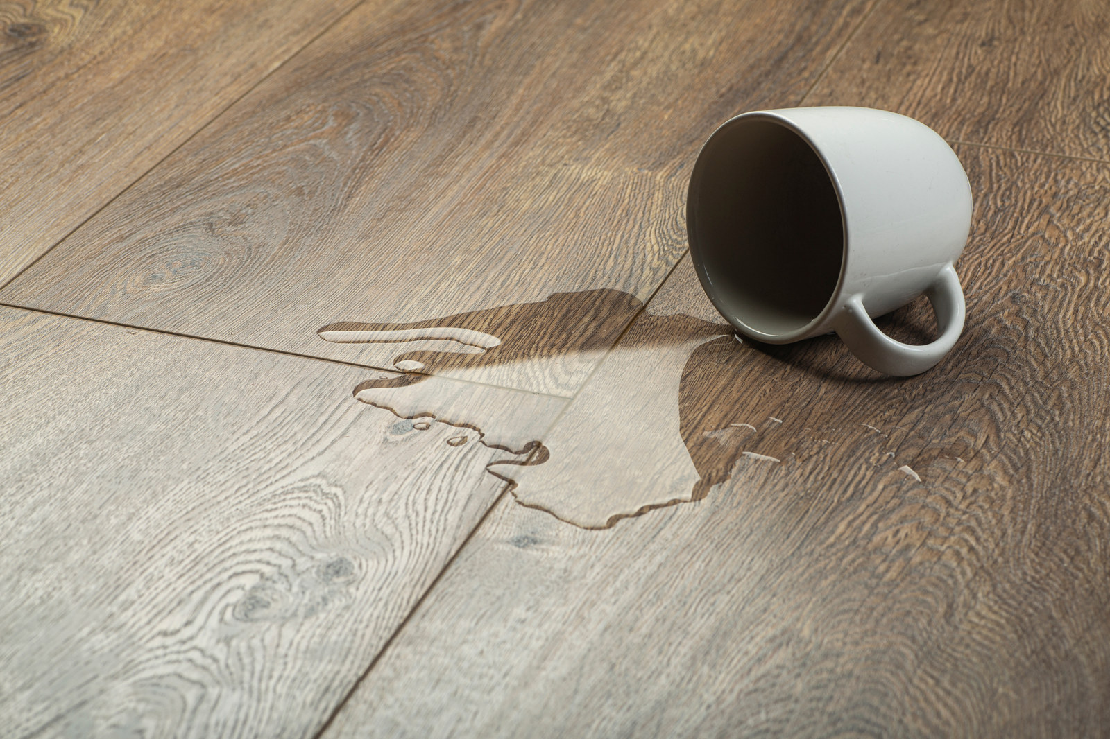 Water beads on a waterproof wood-look floor with a tipped coffee mug